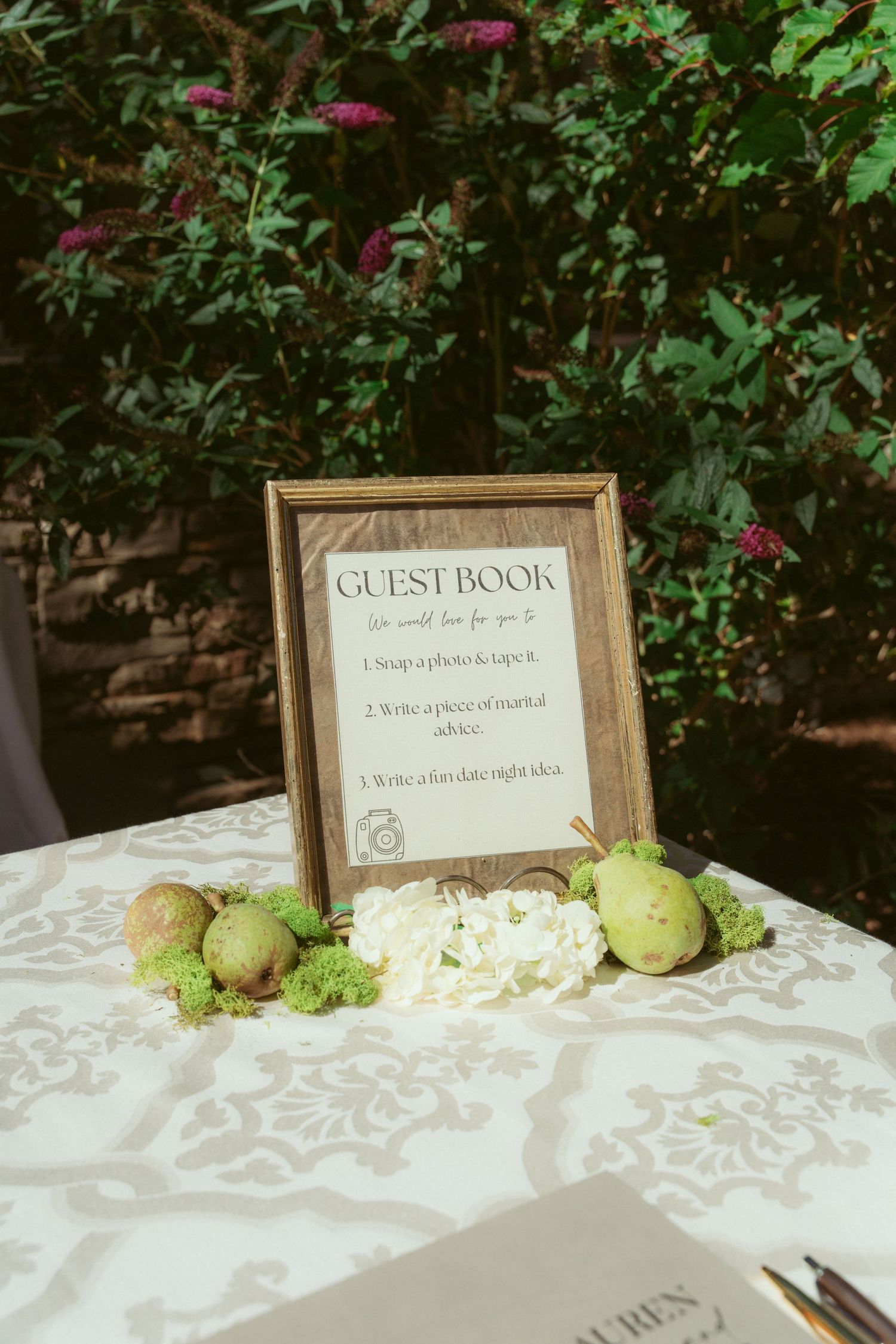 Guest book table with framed sign and decorative pears on white tablecloth.