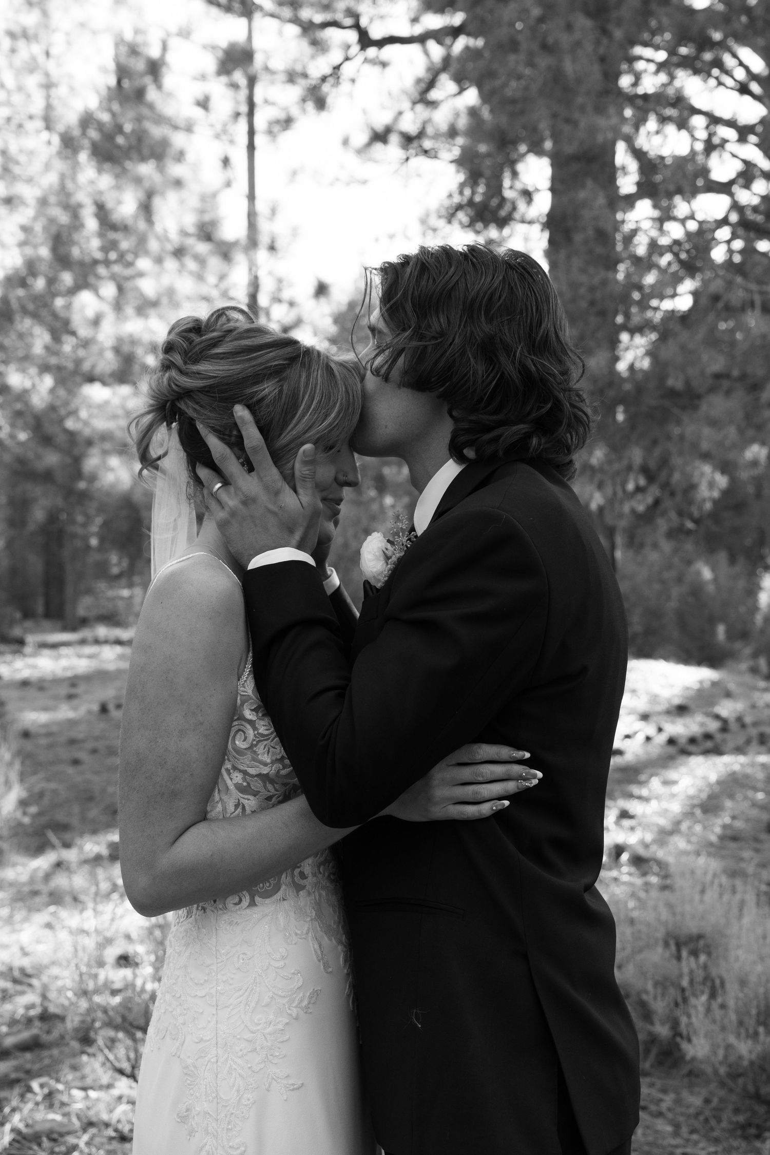 Wedding couple sharing intimate moments among tall pine trees in natural lighting.