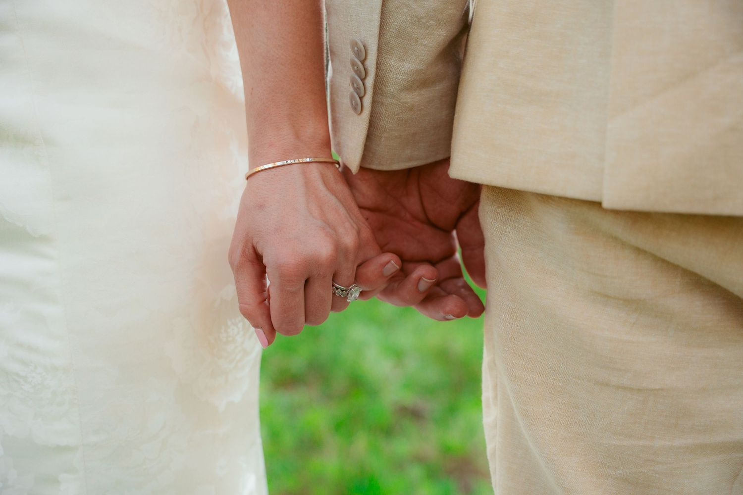 Close-up detail of hands with wedding rings against formal attire.