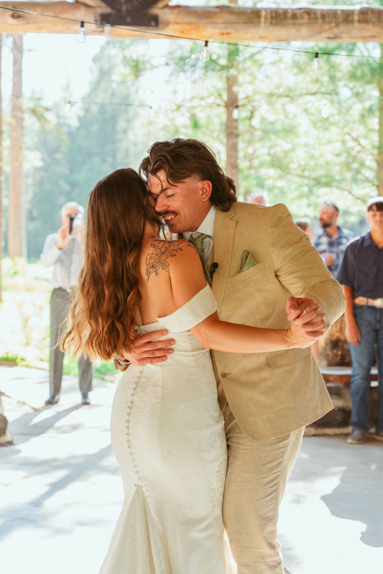 A couple shares a romantic dance in a rustic outdoor pavilion decorated with flowing white curtains.