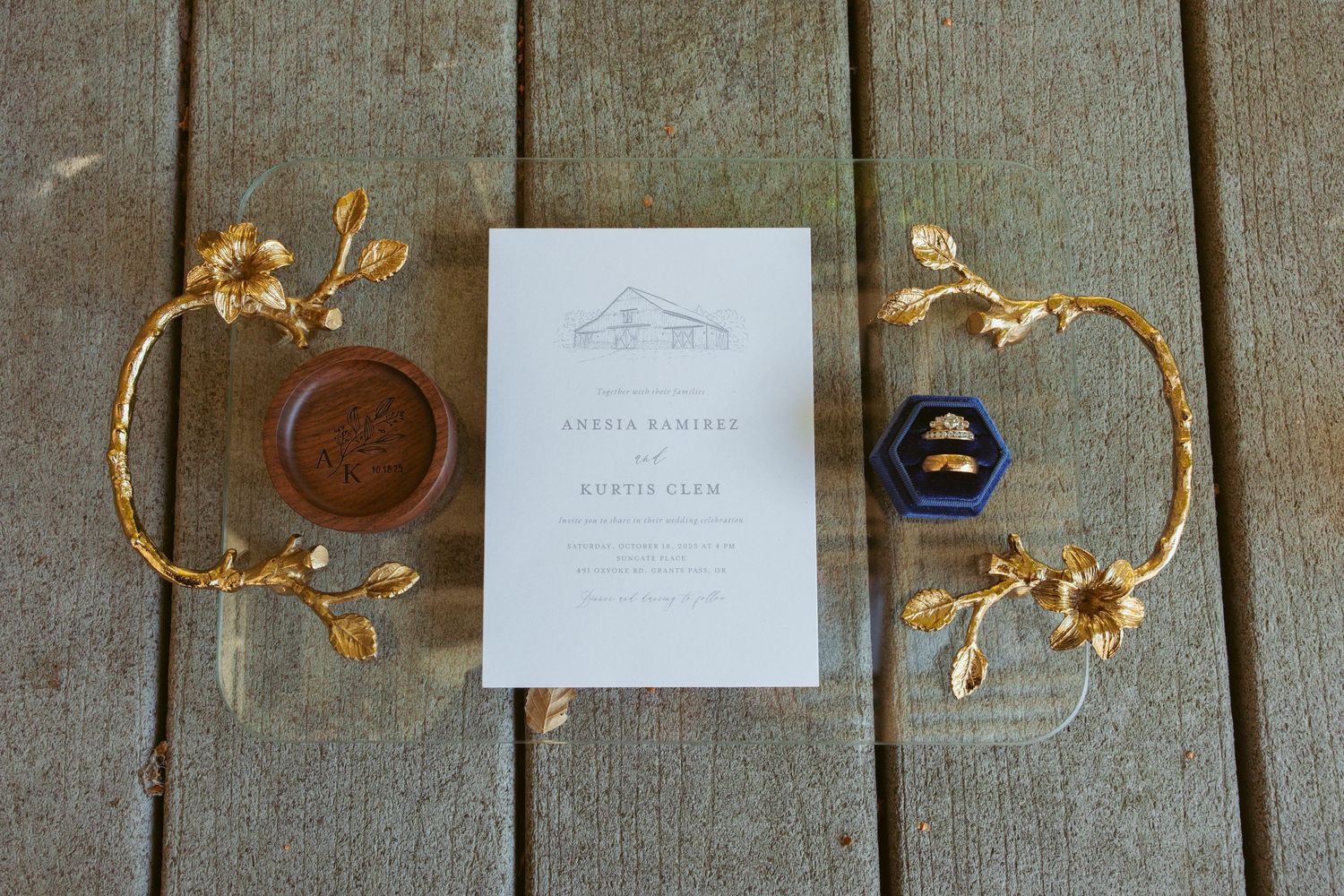 Wedding invitation with gold floral decorations and ring boxes arranged on wooden deck.