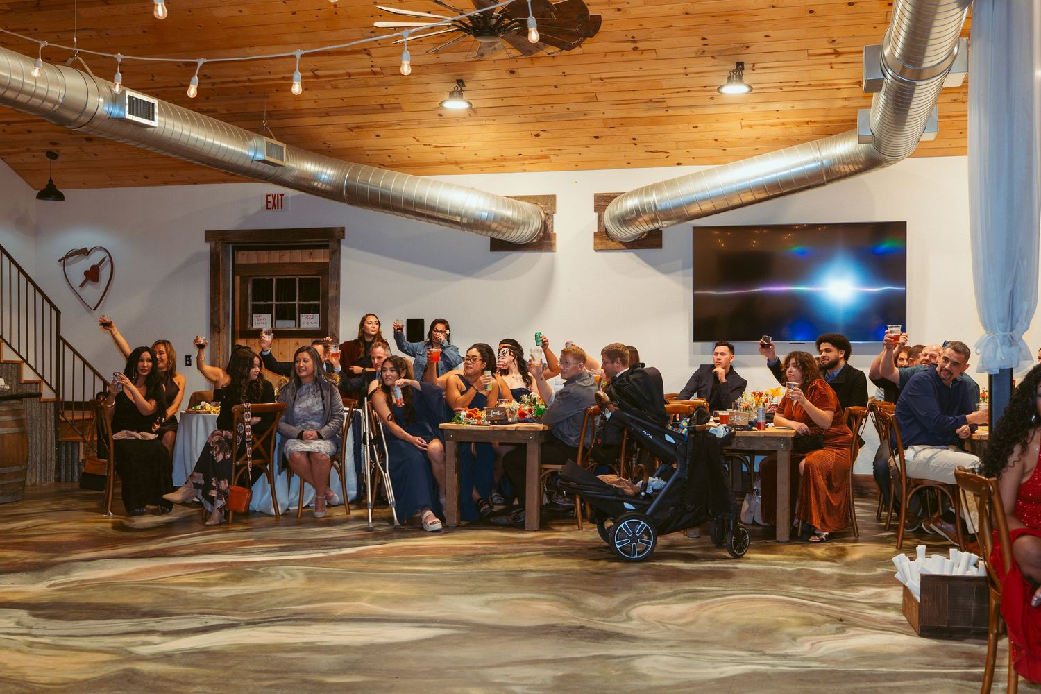 Panoramic view of a wedding reception hall with wooden ceiling and guests seated along tables.