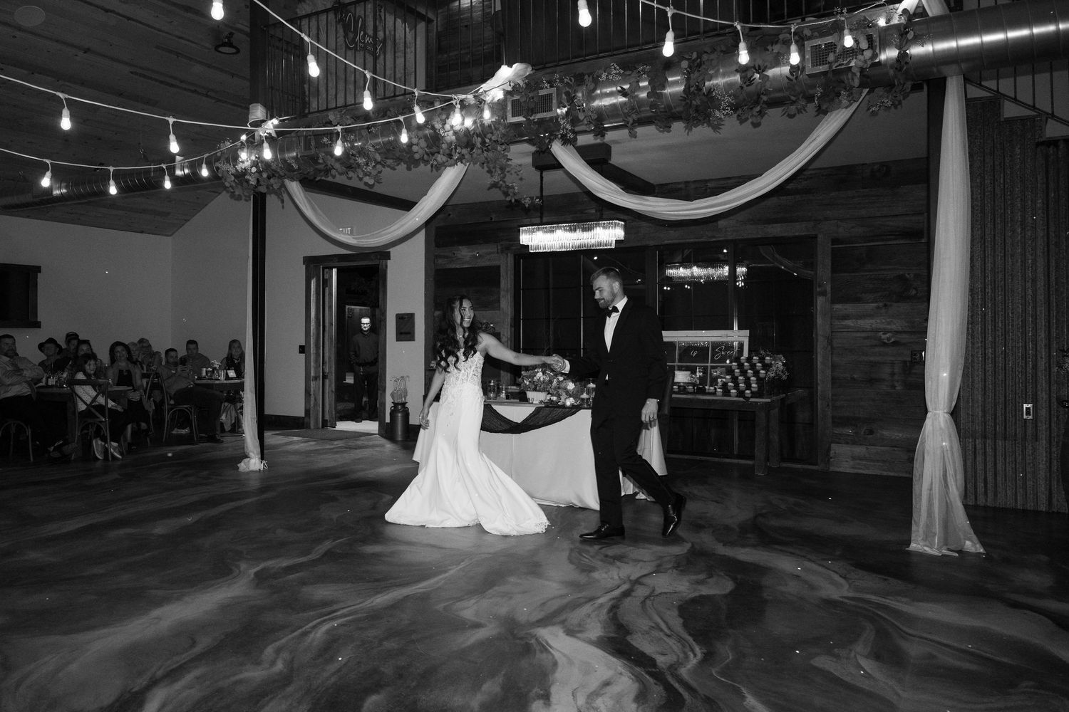 Wedding couple dancing in a dimly lit reception hall decorated with white drapes and string lights.