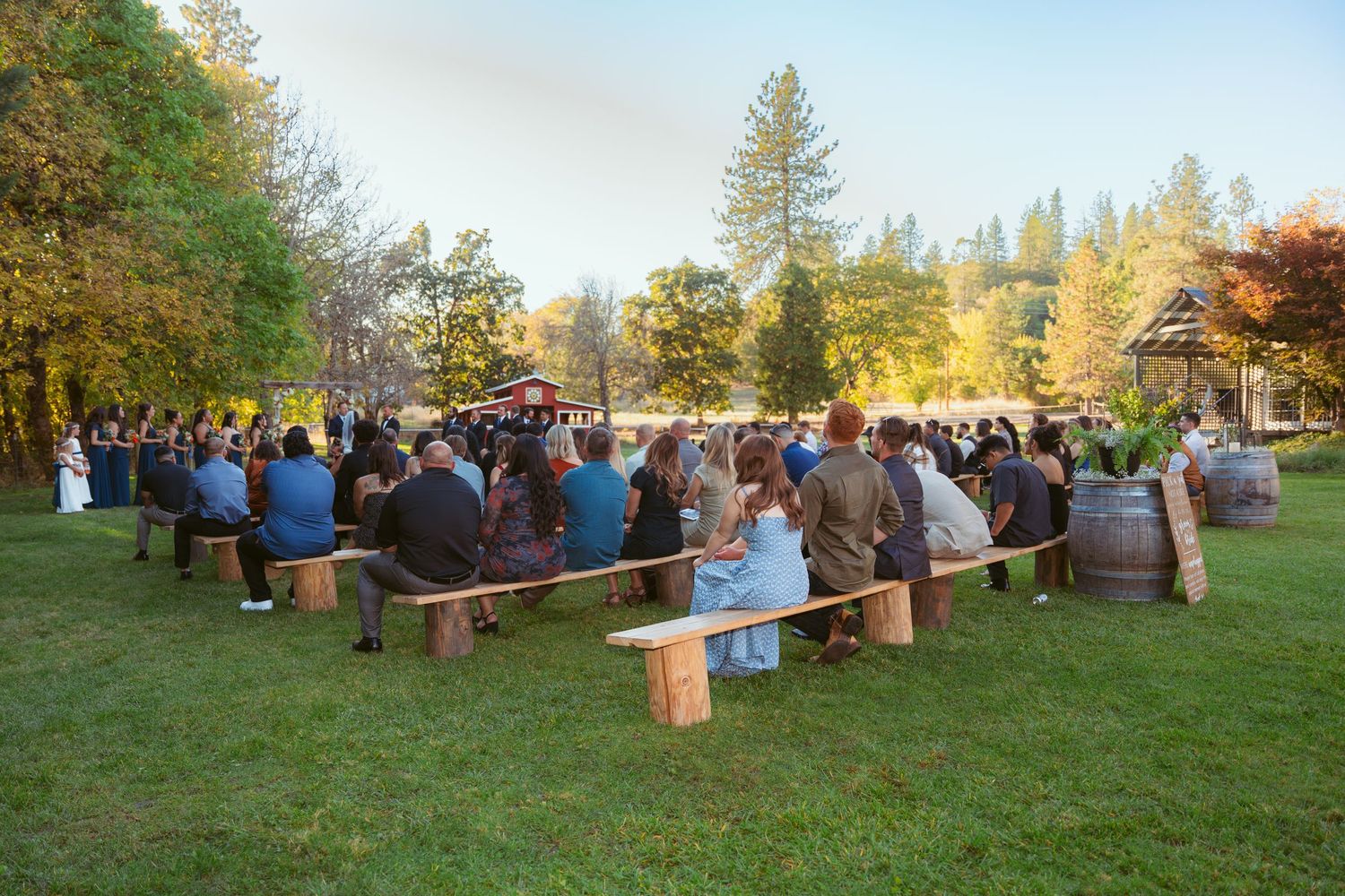 Wedding guests seated on rustic wooden benches during an outdoor autumn ceremony.