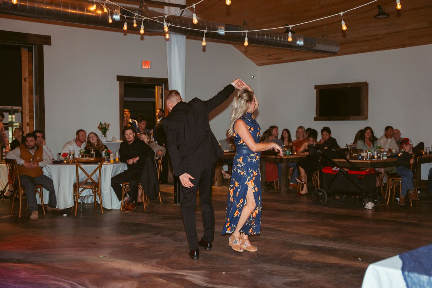 Wedding guests watch as a couple performs a lively dance move on the reception floor.