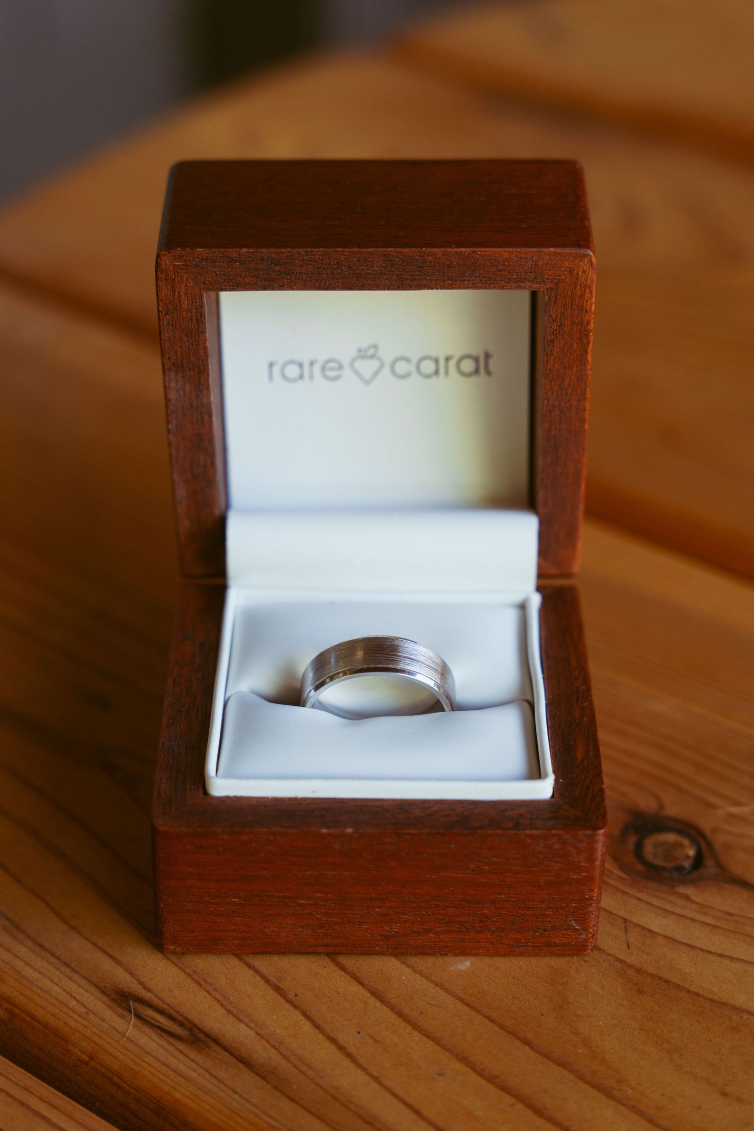 Wooden ring box with Rare Carat branding displaying a silver wedding band.