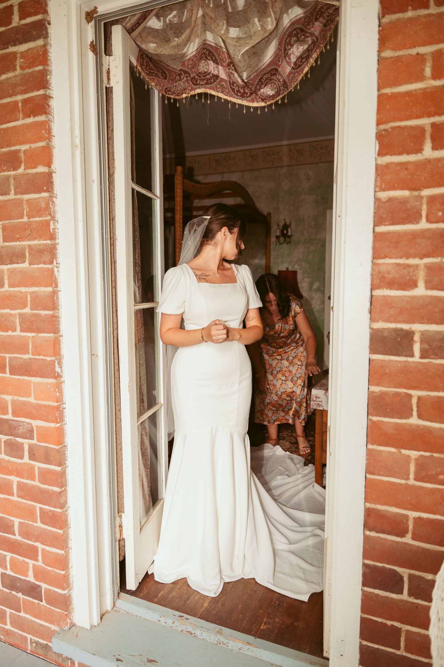 Elegant white wedding dress framed in a doorway with exposed brick exterior.