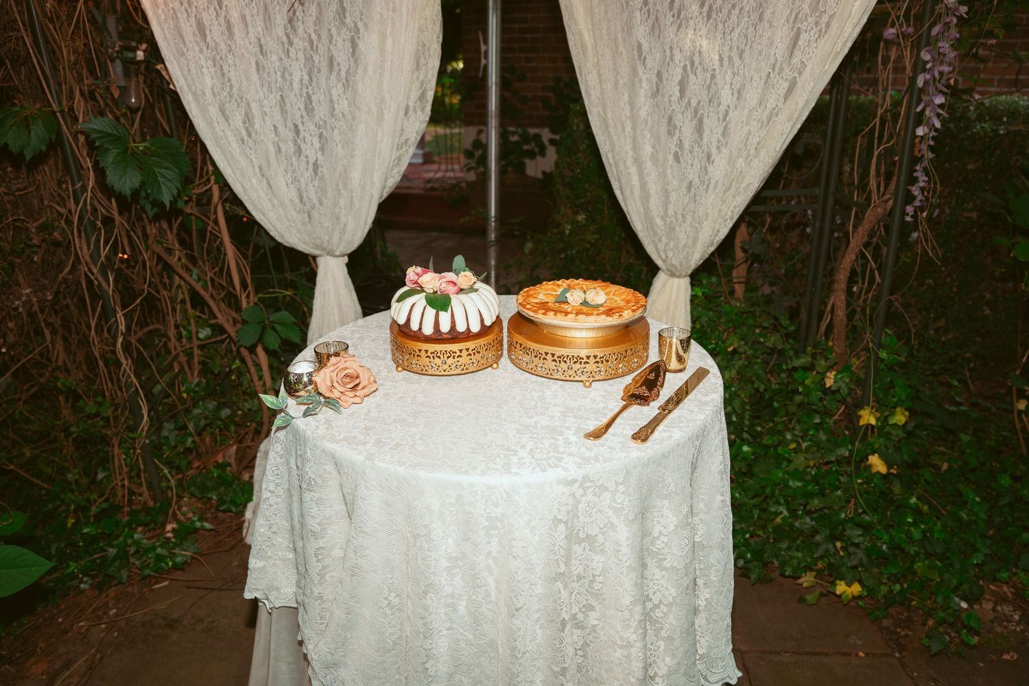 Wedding dessert table with white draping and cakes displayed on elegant stands.