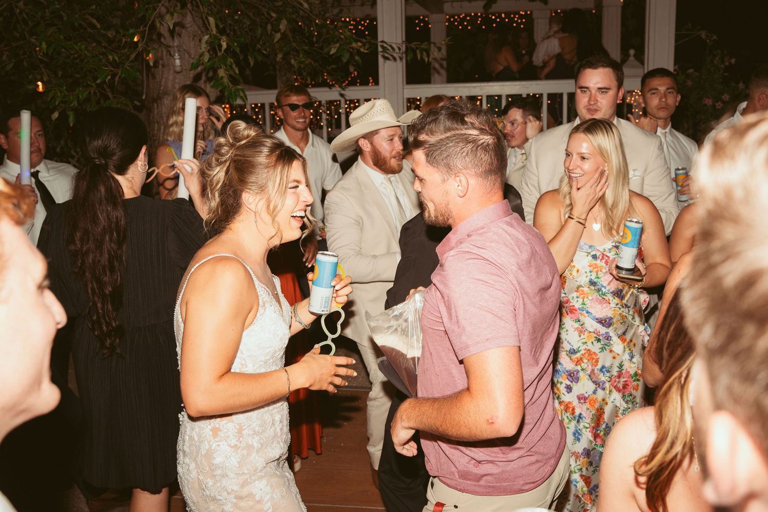 Wedding guests dancing and celebrating under romantic string lights at outdoor reception.
