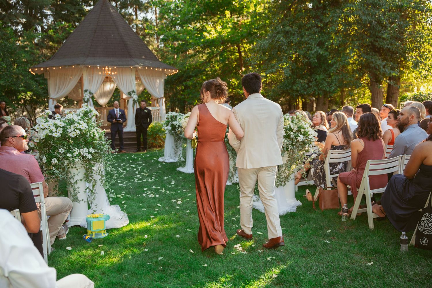 Garden wedding ceremony with guests gathered on a green lawn during golden hour.
