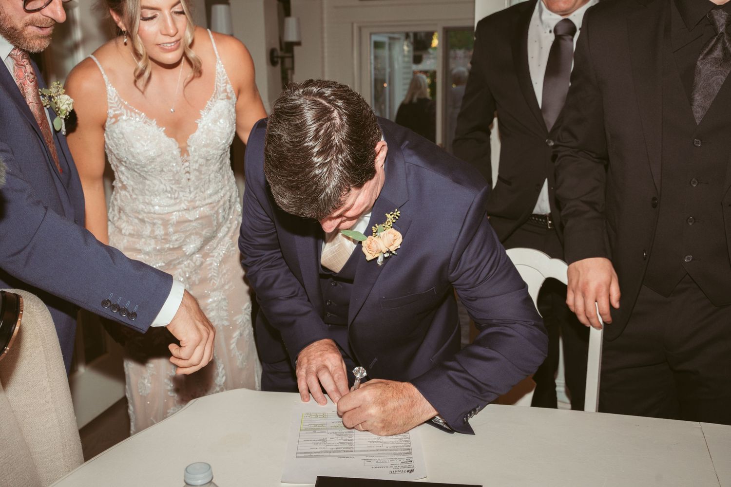 Wedding ceremony participants signing official documents at an elegant indoor venue.