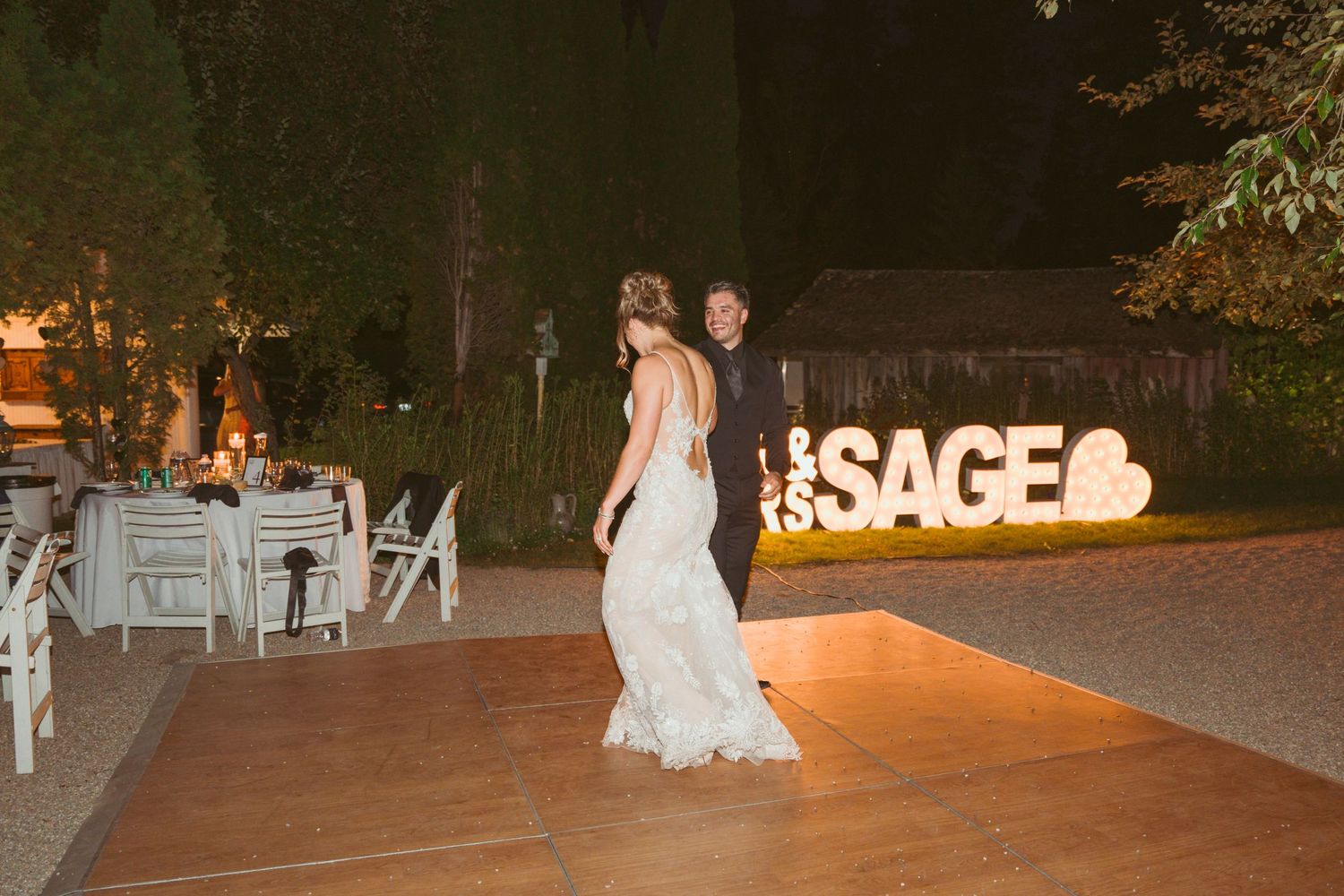 Nighttime wedding celebration with illuminated SAGE signage and guests on a patio.