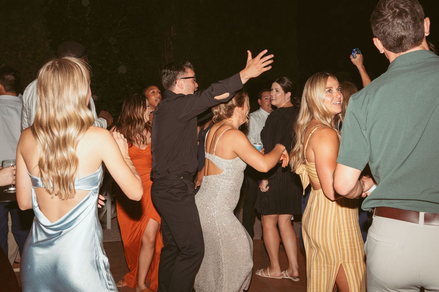 Wedding reception guests dancing and celebrating on a dimly lit dance floor.