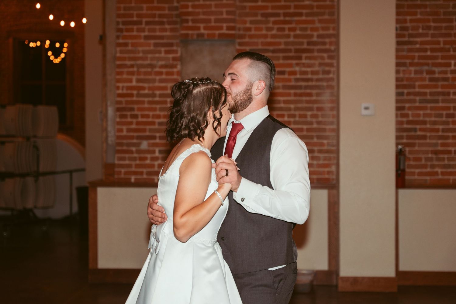 A couple laughs together during their first dance in a rustic brick-walled reception venue.
