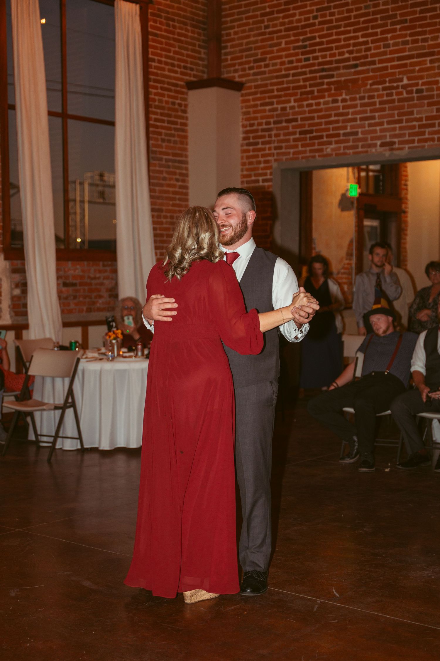 Dancers moving gracefully across hardwood floor in brick-walled reception venue.
