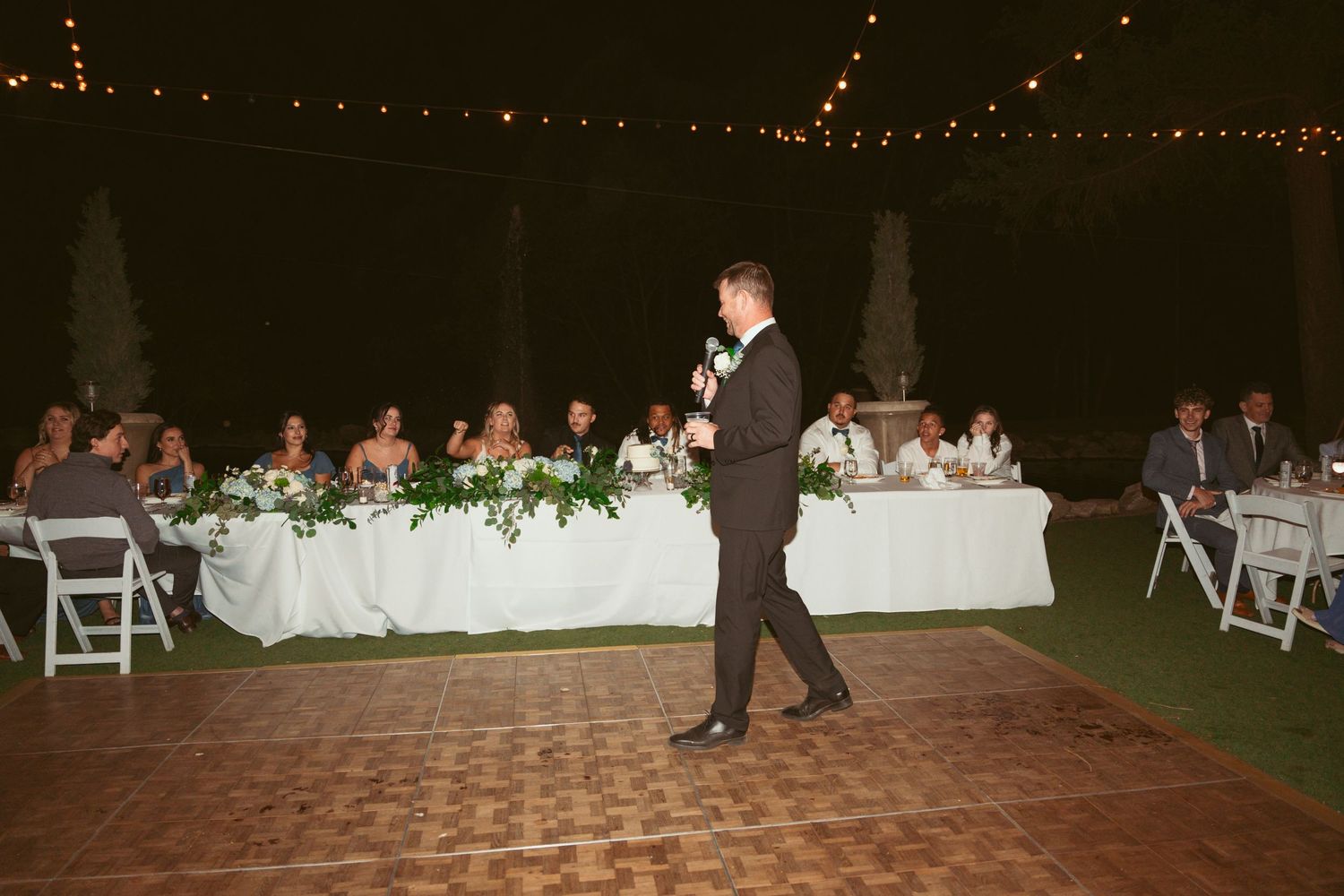 Outdoor wedding reception setup with string lights and white folding chairs.
