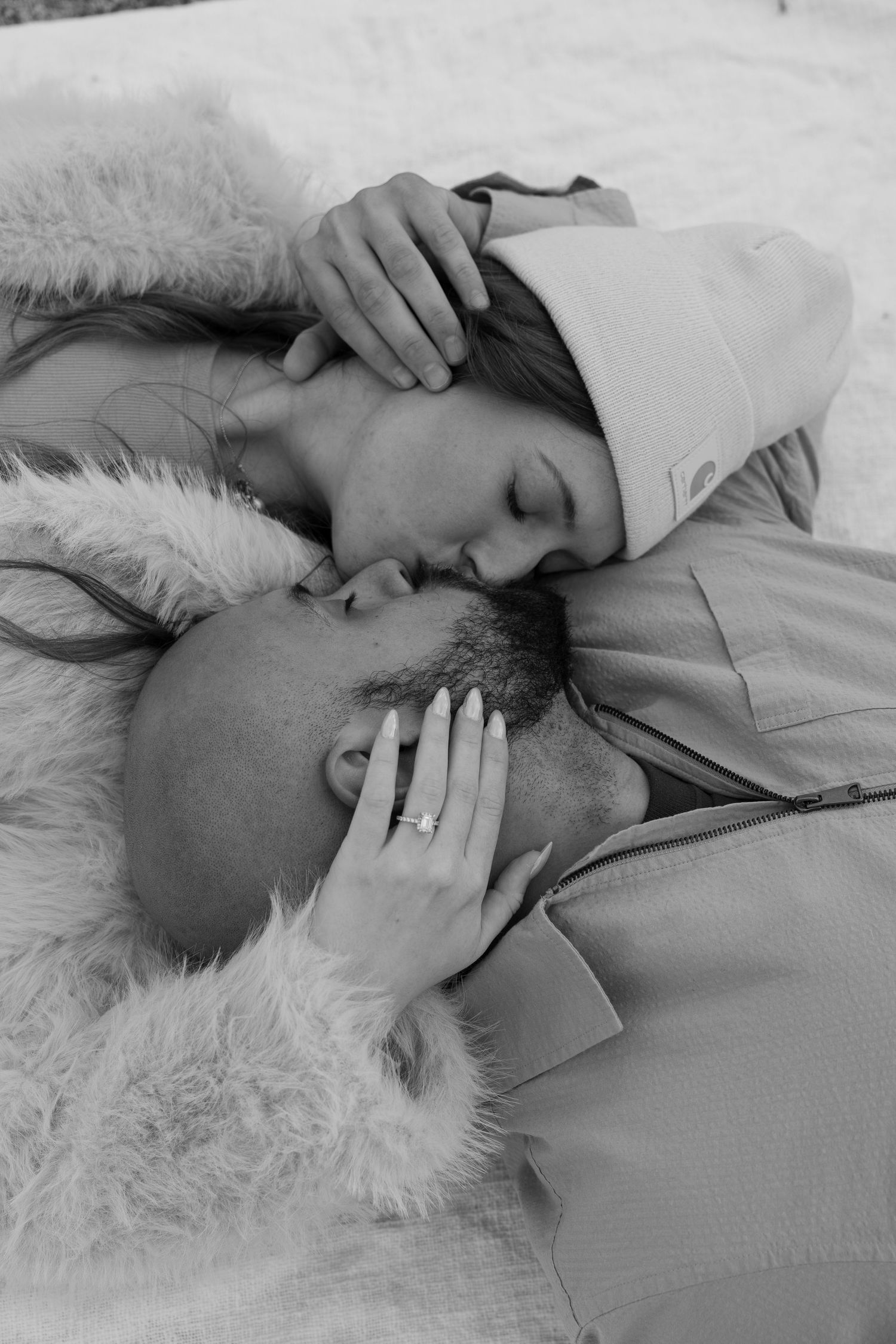 Couple sharing intimate moments while lying on white fur blanket in black and white photography.