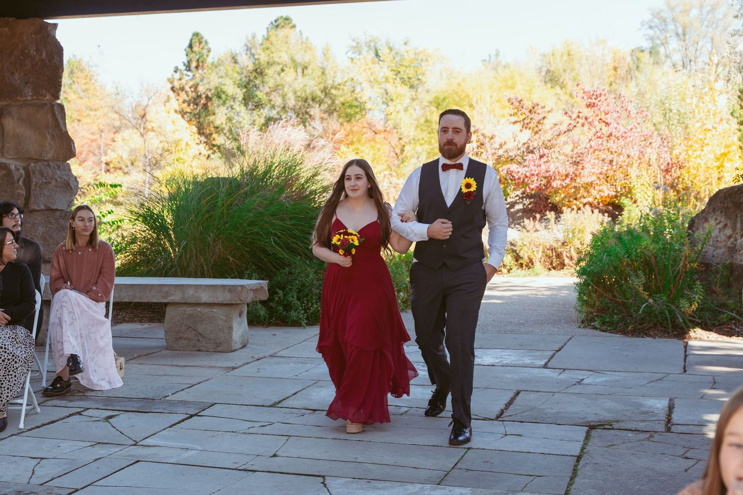 Guests mingle during an outdoor celebration with fall colors visible in the background.