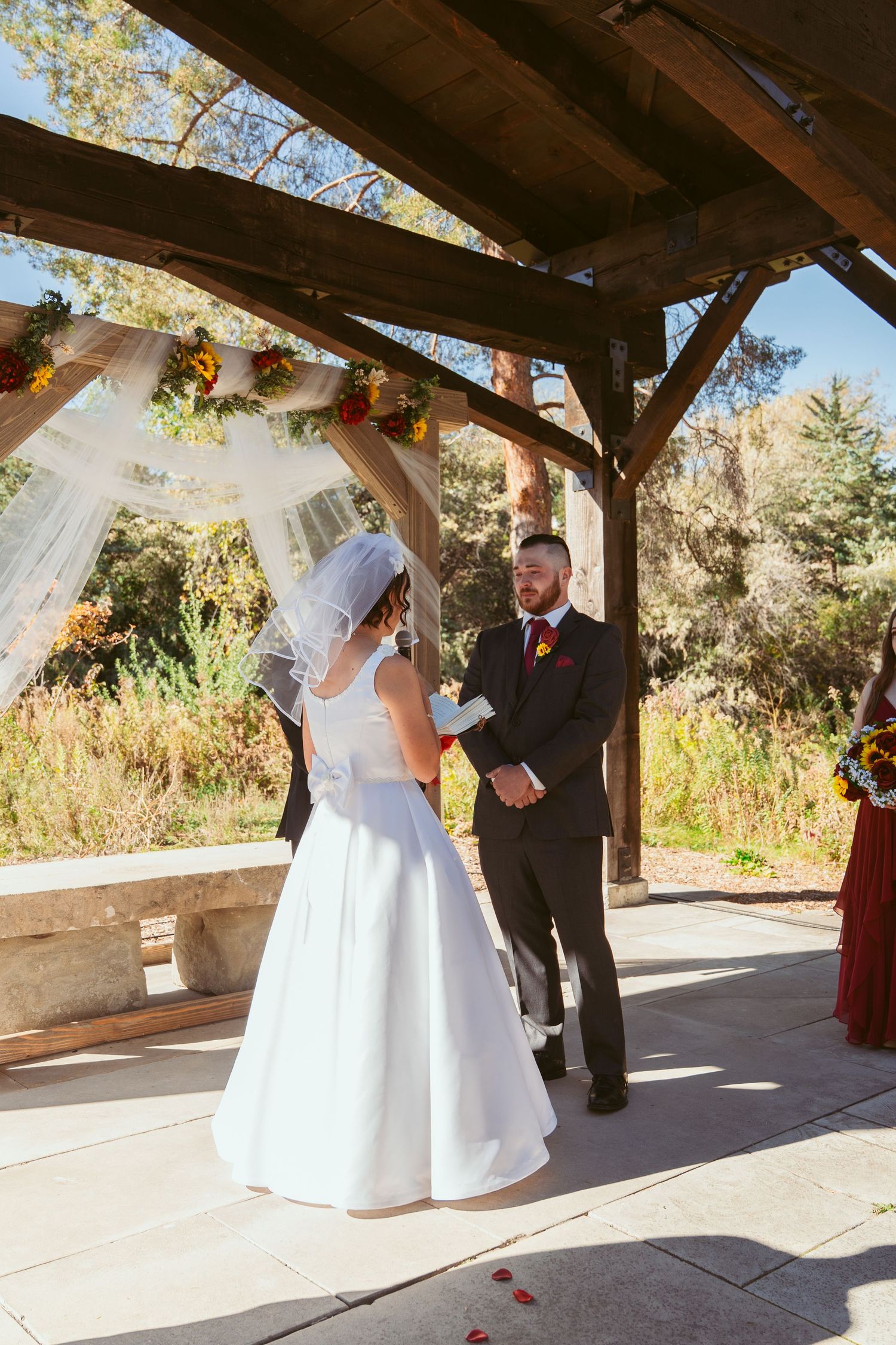 Autumn wedding ceremony with floral decorations under wooden pavilion during vow exchange.