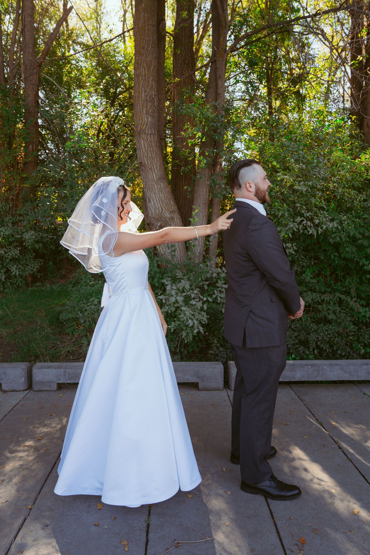 A bride reaches out to tap her groom's shoulder during their first look wedding moment.