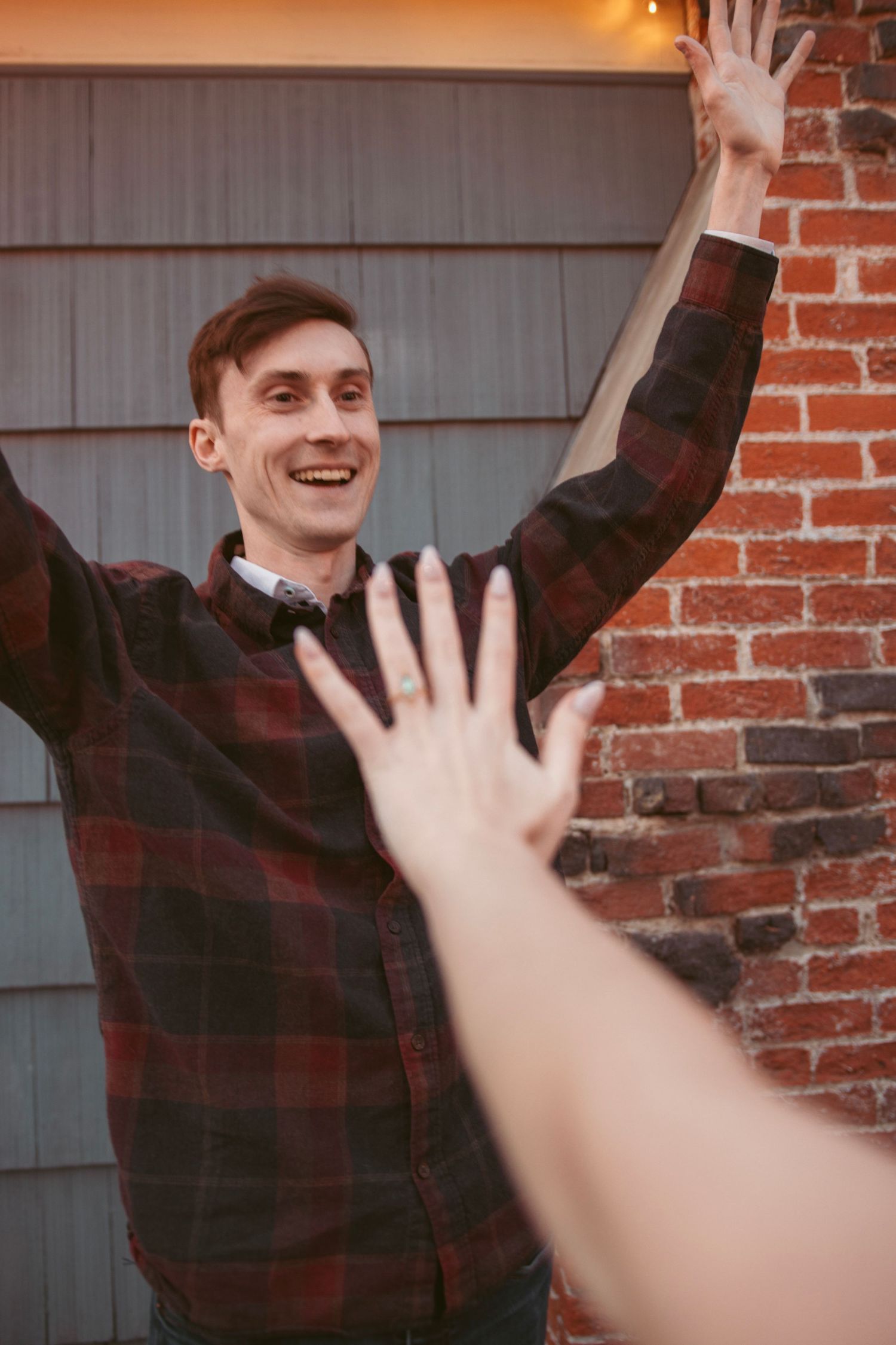 Joyful celebration with raised hands against brick wall background.