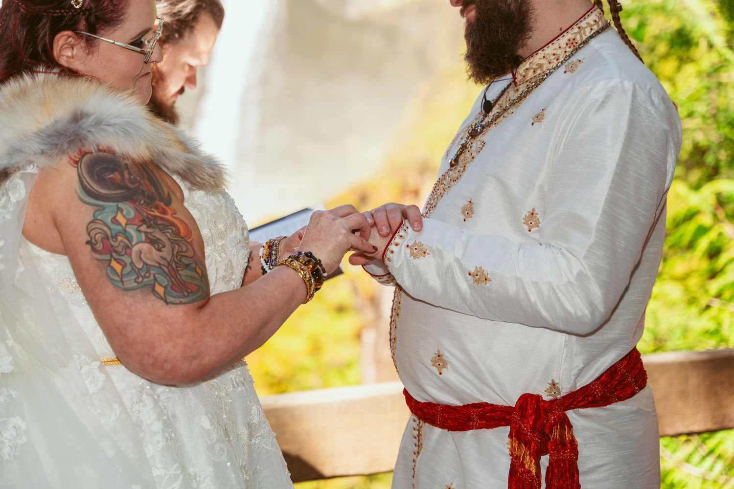 A couple shares a romantic moment in white and red wedding attire outdoors.