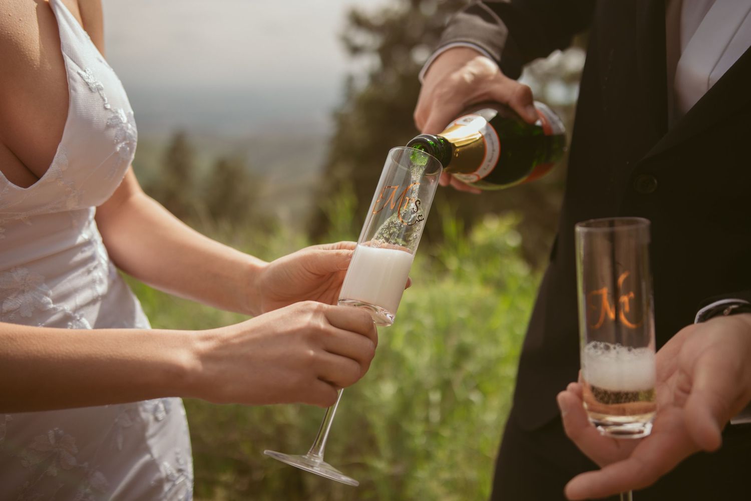 Hands clink champagne glasses together during an outdoor wedding celebration.