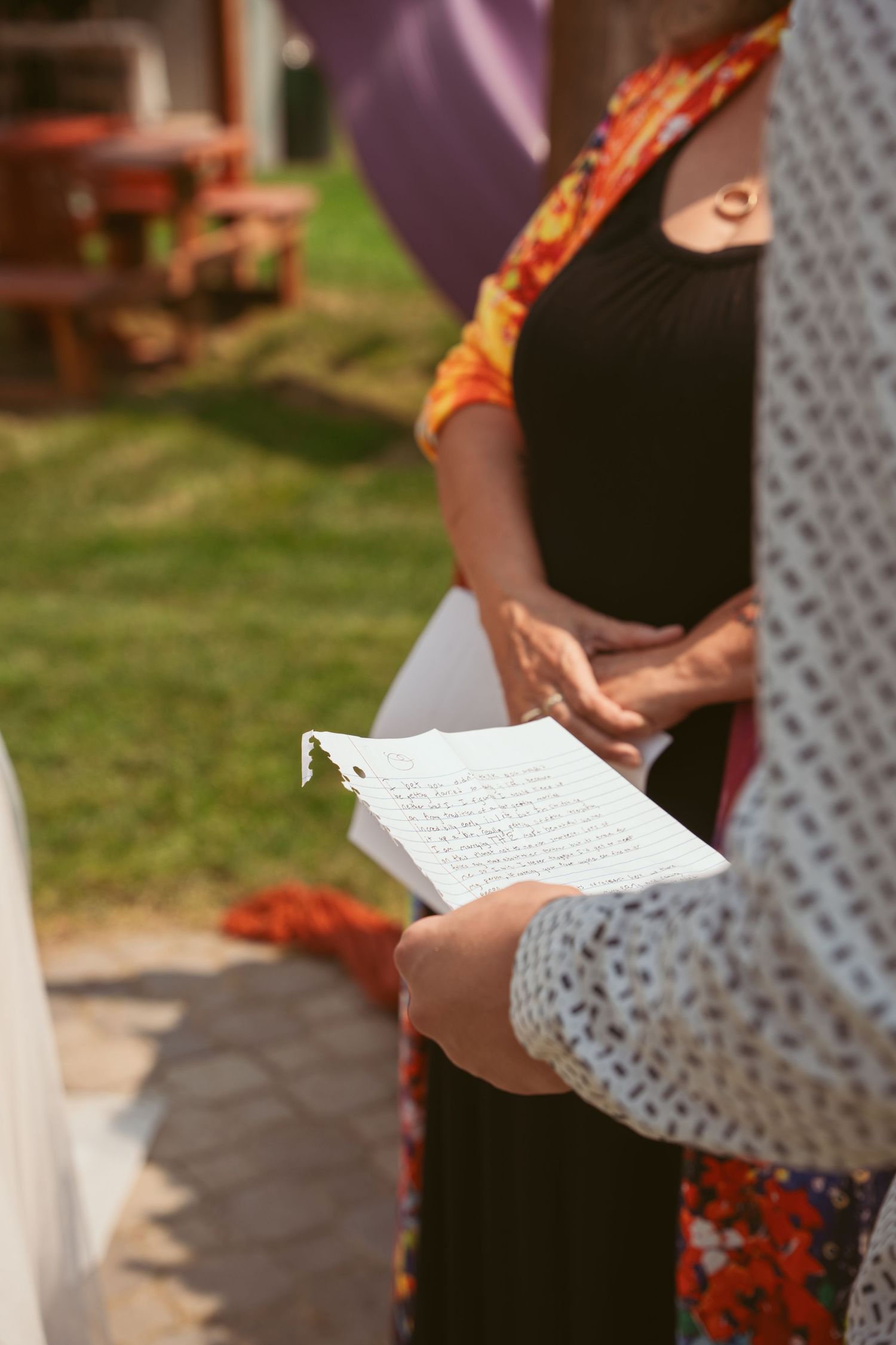 Hands holding papers during an outdoor ceremony with purple and orange decor.