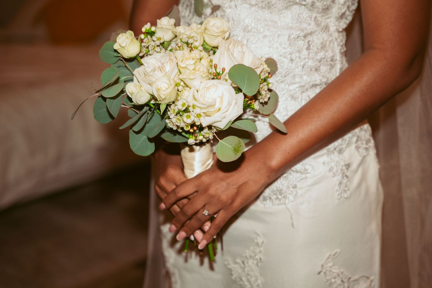 White bridal bouquet with roses and eucalyptus leaves against a lace wedding dress.