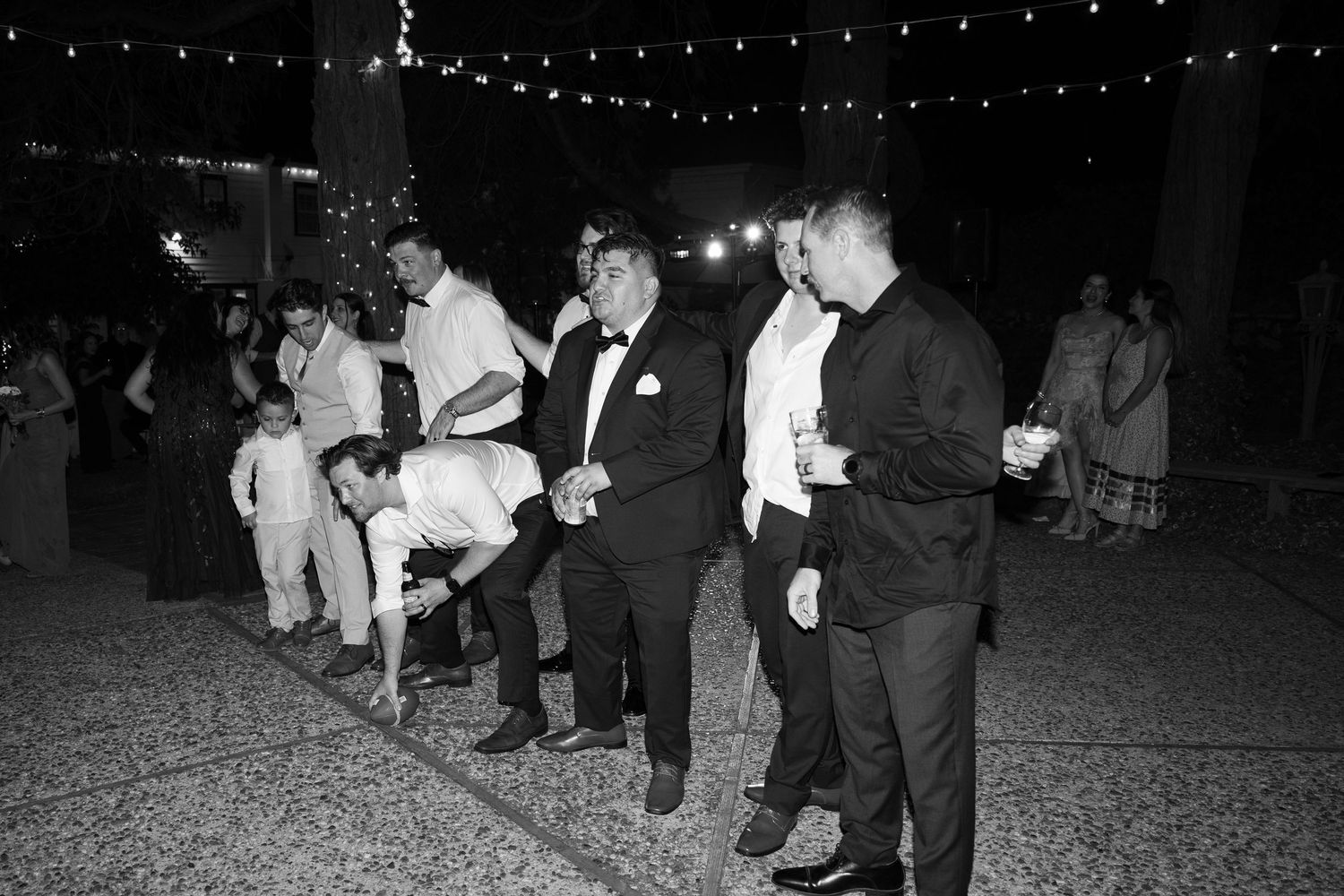 Guests enjoying a festive nighttime outdoor wedding reception with string lights overhead.