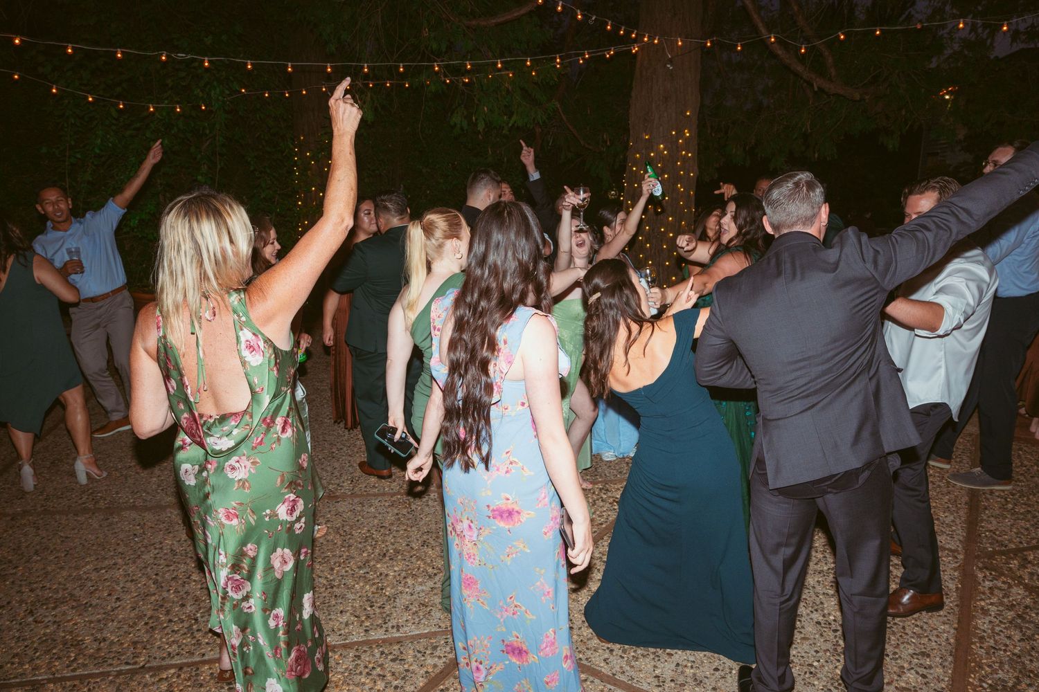 Wedding guests dancing and celebrating on a patio under string lights at night.