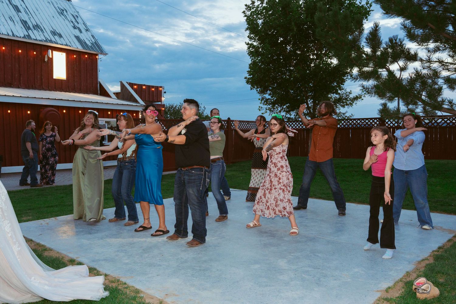 Group dancing in formation at an outdoor wedding with a red barn in the background.