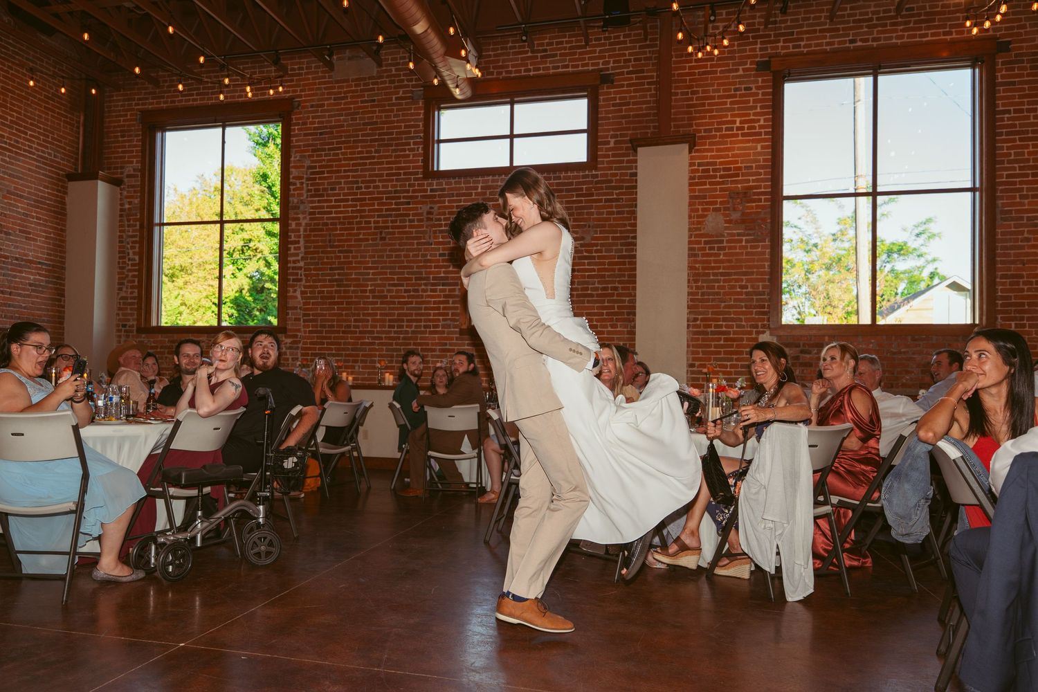 Couple dancing at wedding reception in rustic brick venue with decorative lighting.