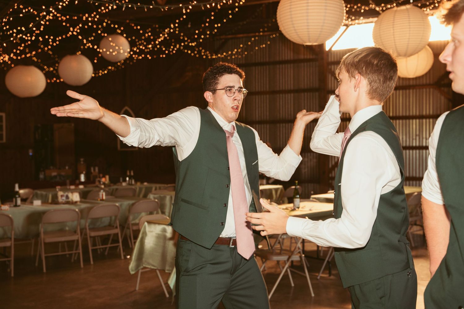 Lively dancing and celebration under string lights and paper lanterns at a rustic wedding venue.