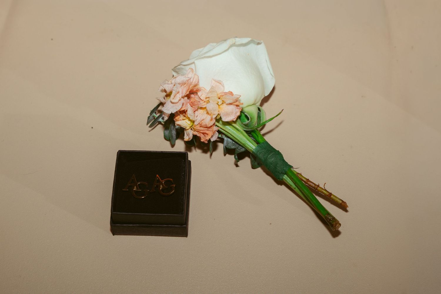 Wedding boutonniere with white and peach flowers next to a black ring box.