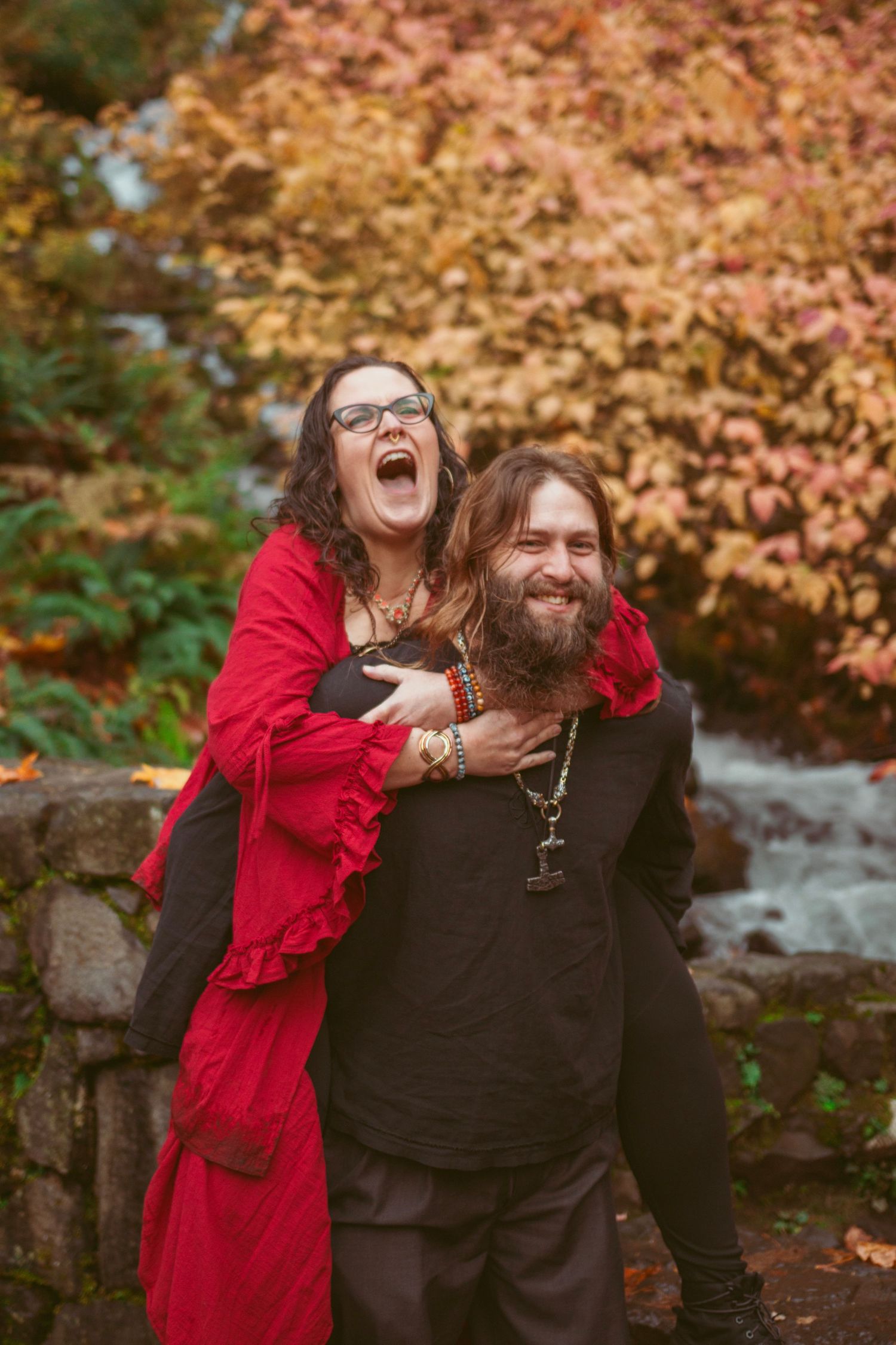 Candid laughter captured during autumn photoshoot with waterfall and fall colors in background.