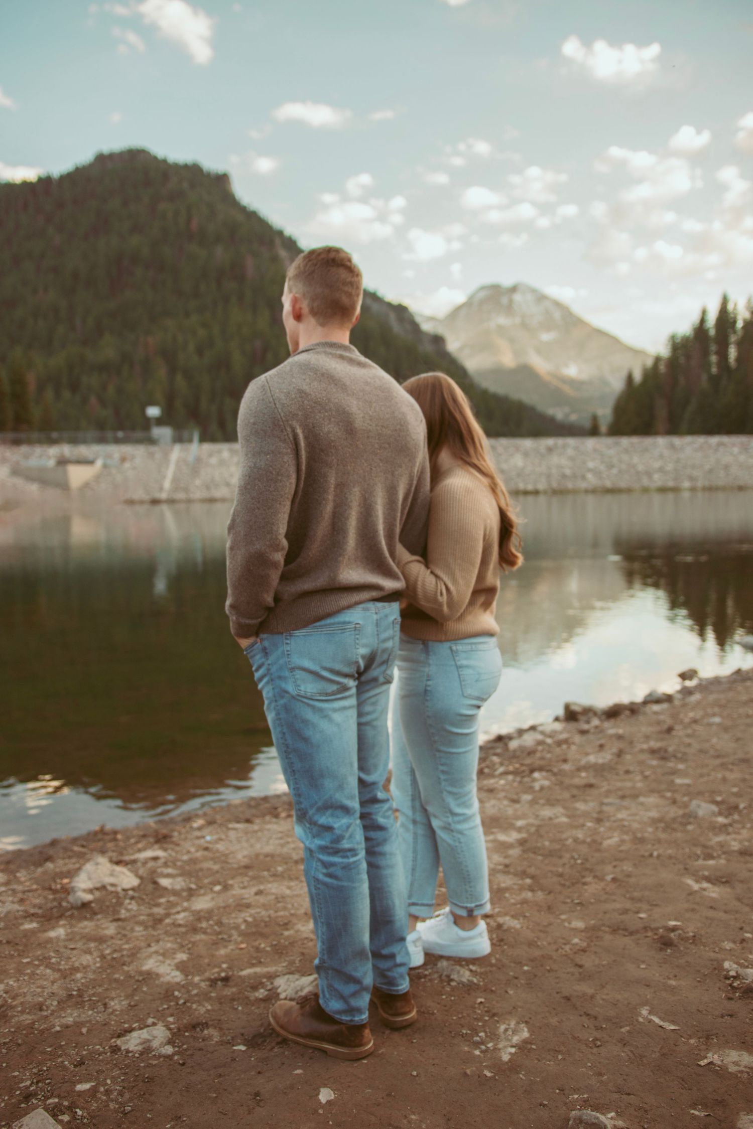 Couple in casual wear standing together overlooking a peaceful mountain lake.