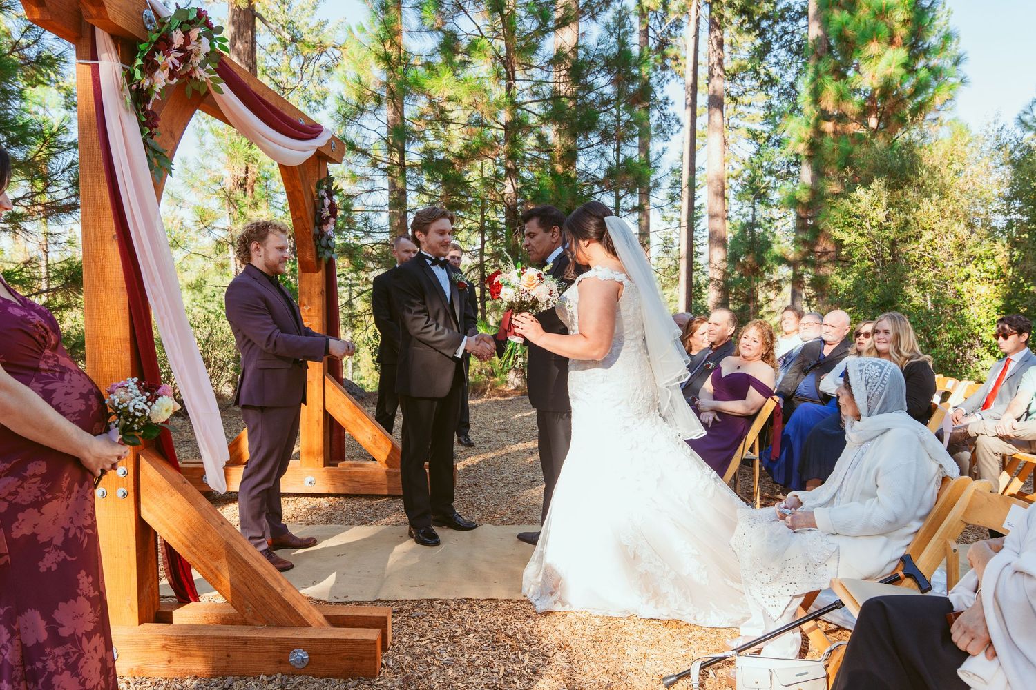 Couple celebrates their marriage in a rustic outdoor ceremony surrounded by pine trees.