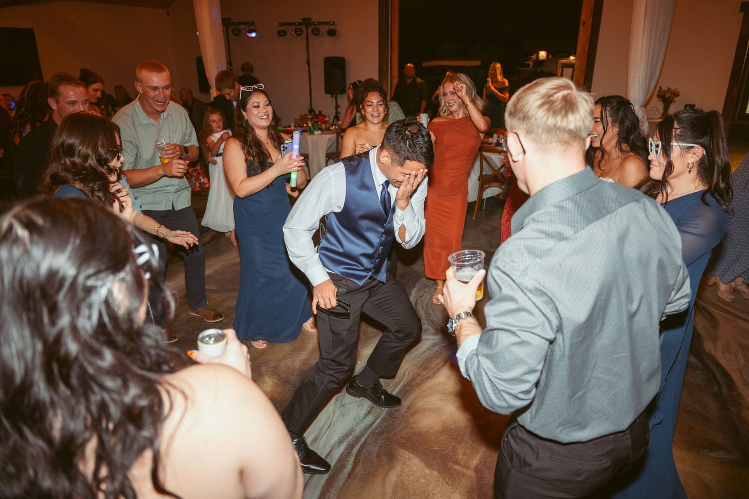 Wedding guests dance and celebrate with glow sticks on a wooden dance floor.