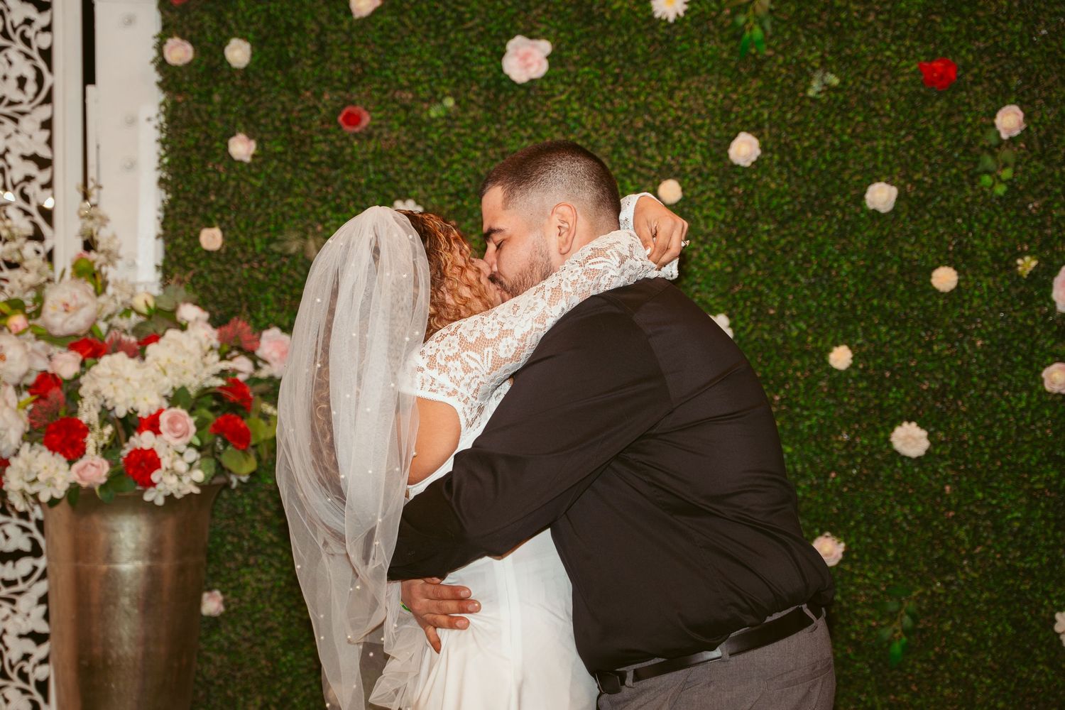 Newlyweds share a romantic moment in front of a green hedge wall decorated with roses.