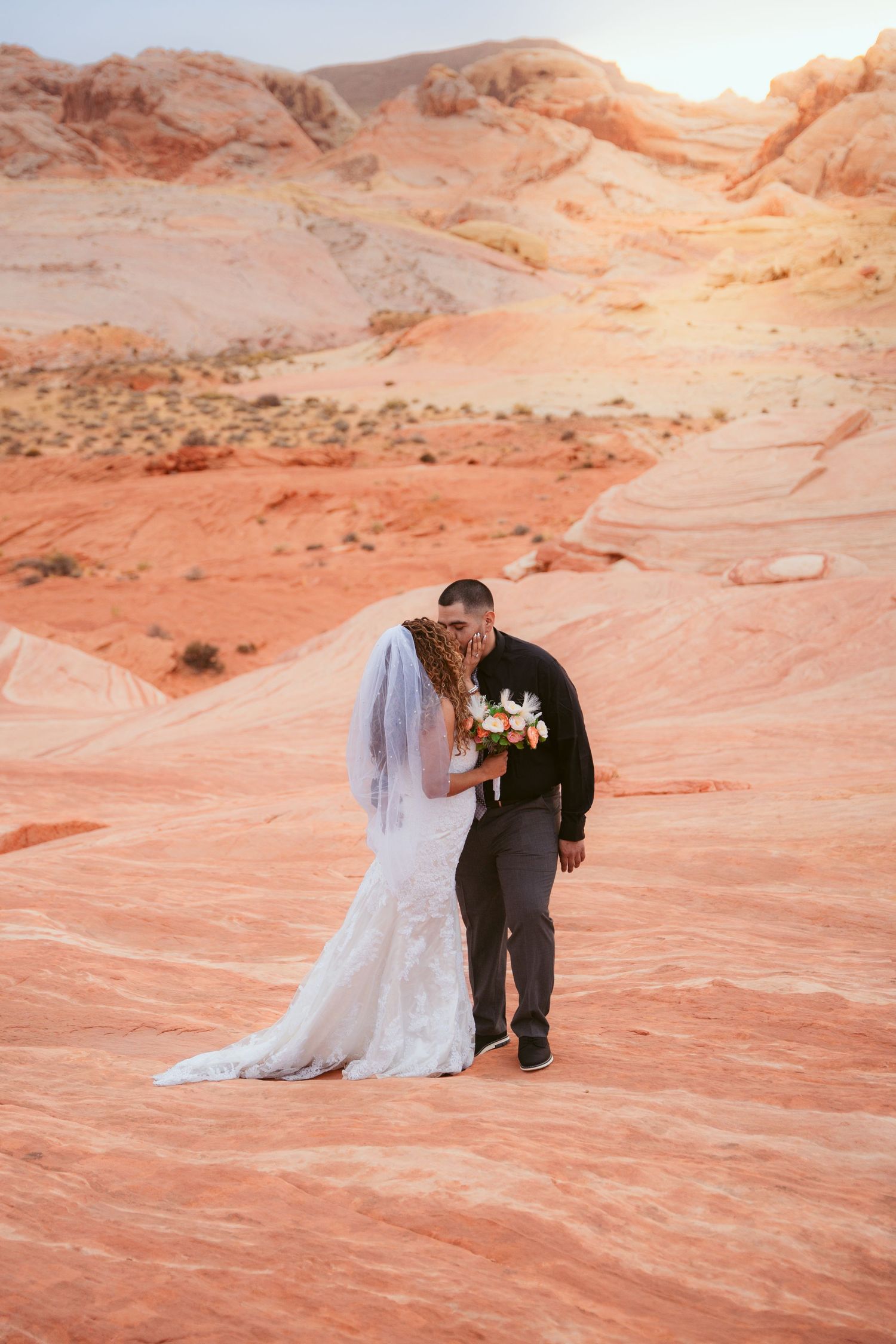 A wedding photoshoot on sweeping red rock formations in the desert landscape.