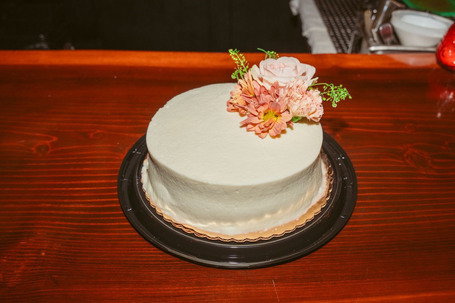 Simple white wedding cake with pink floral decorations displayed on wooden table surface.