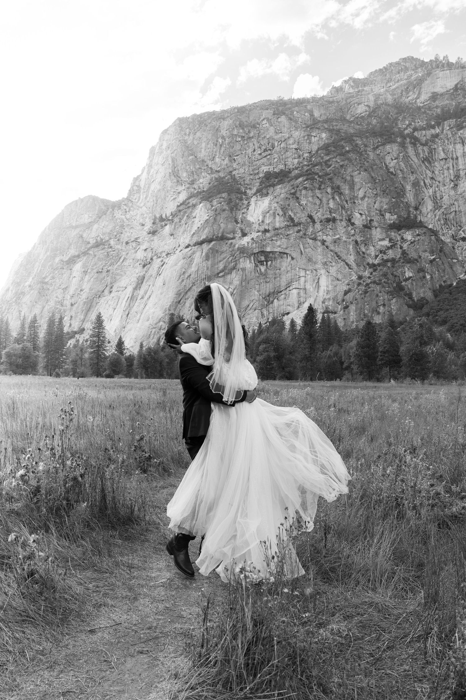 Wedding couple embracing in a meadow with Yosemite's iconic granite cliffs as backdrop.