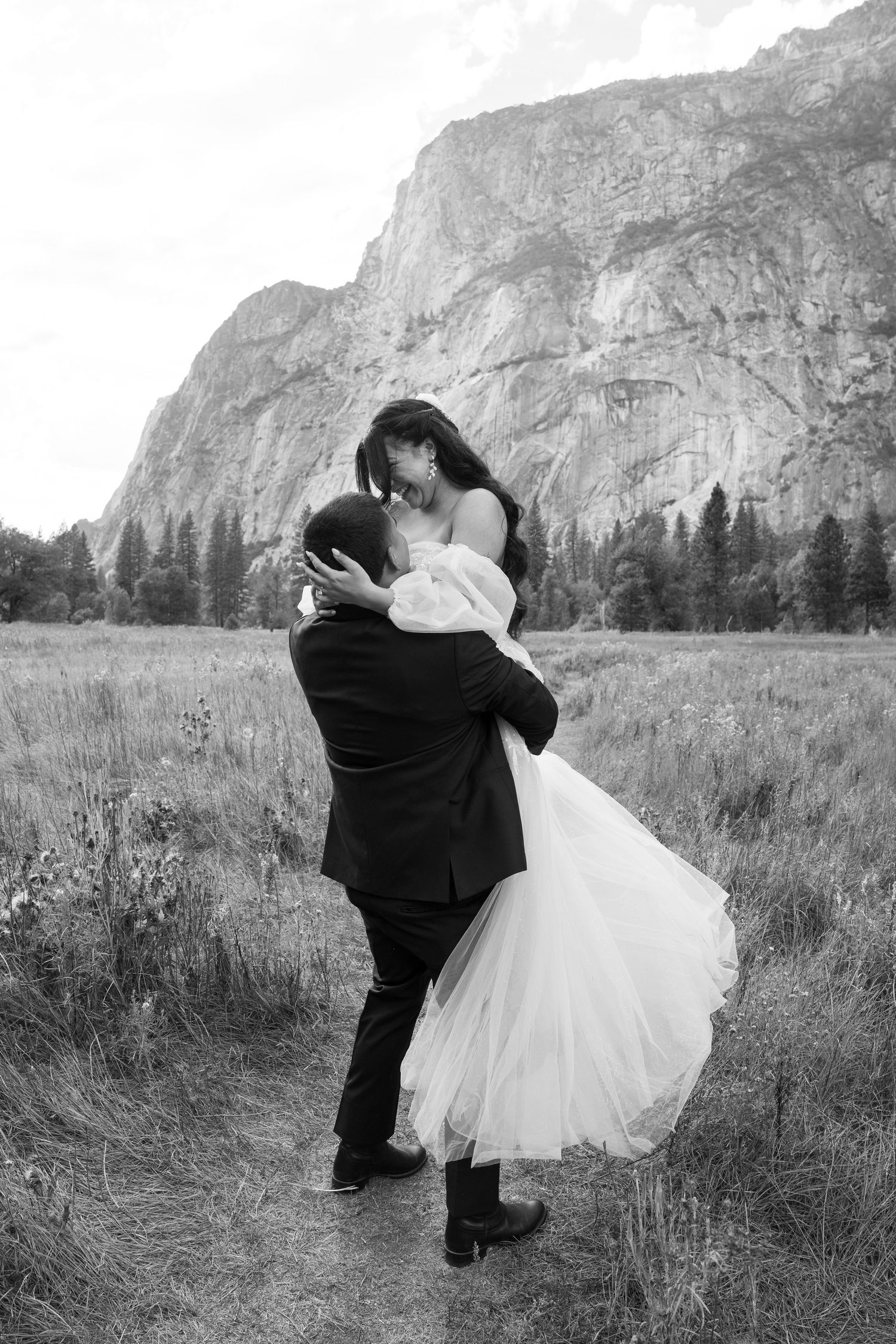 Black and white romantic dip pose in Yosemite meadow with towering cliff backdrop.