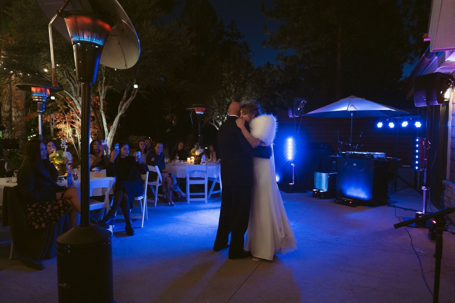 A romantic evening wedding reception venue illuminated with blue uplighting and outdoor decor.