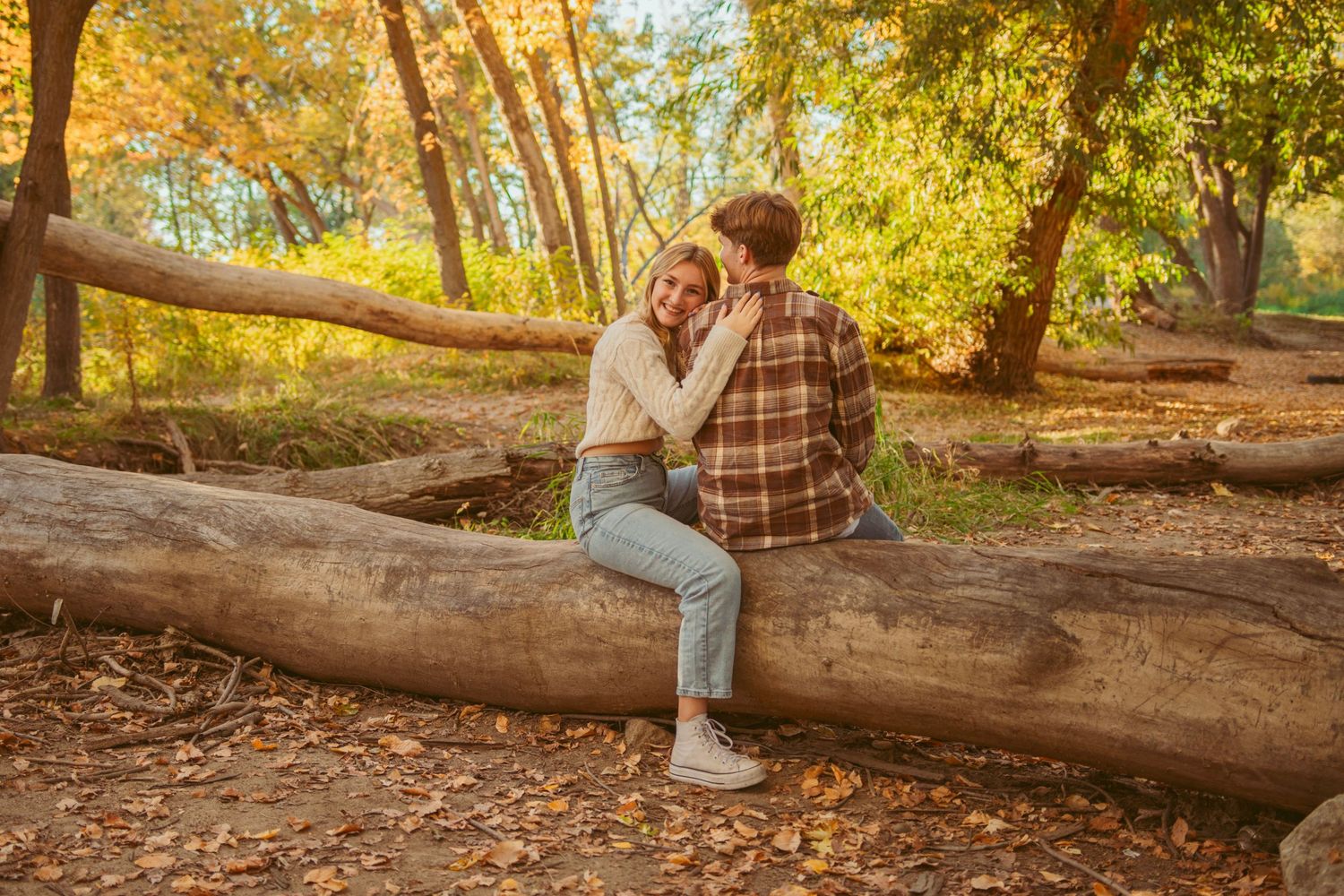 Casual outdoor portraits on fallen log in sunlit forest setting.