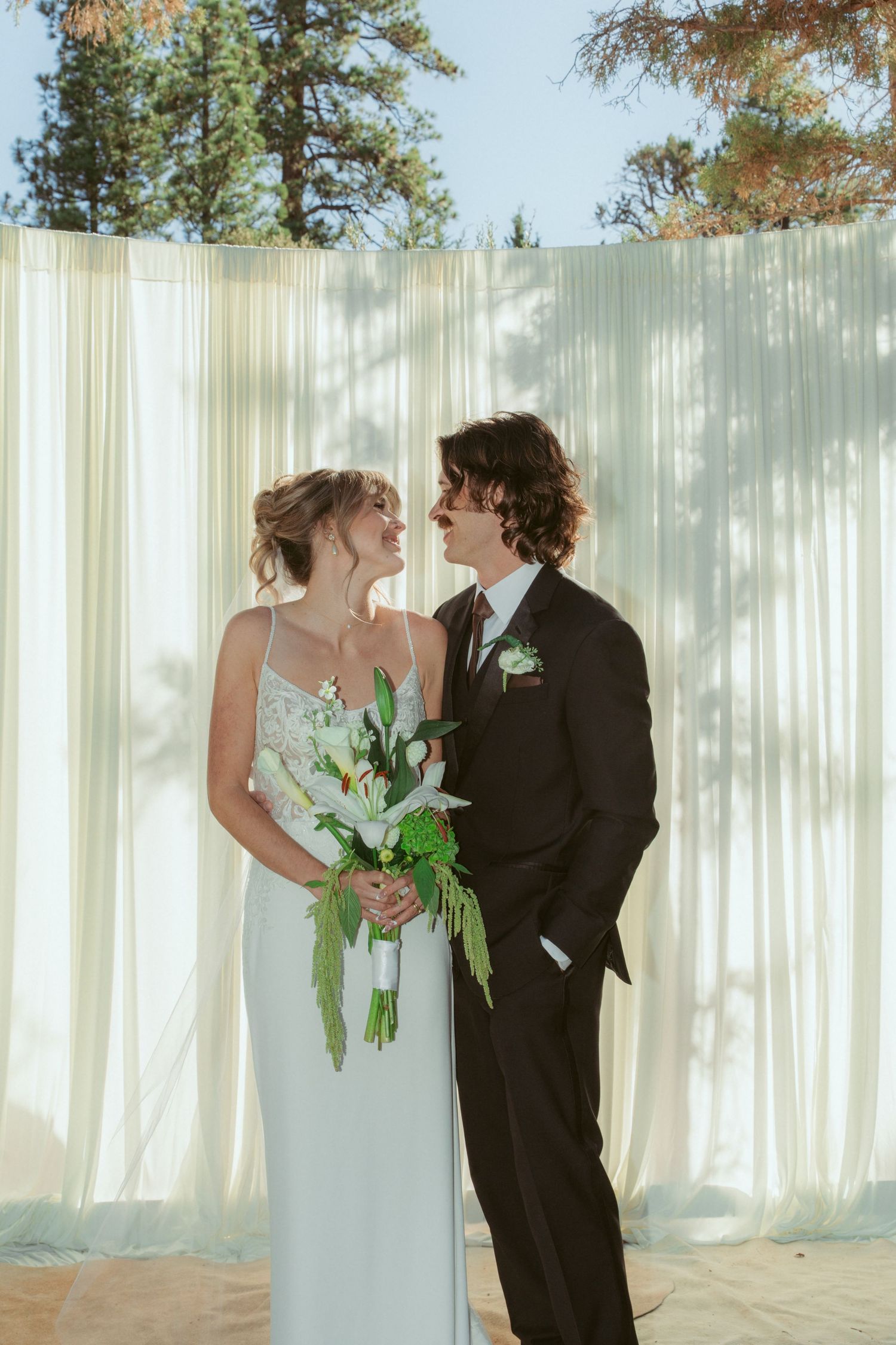 A romantic wedding portrait of a couple in front of white curtains with natural sunlight.