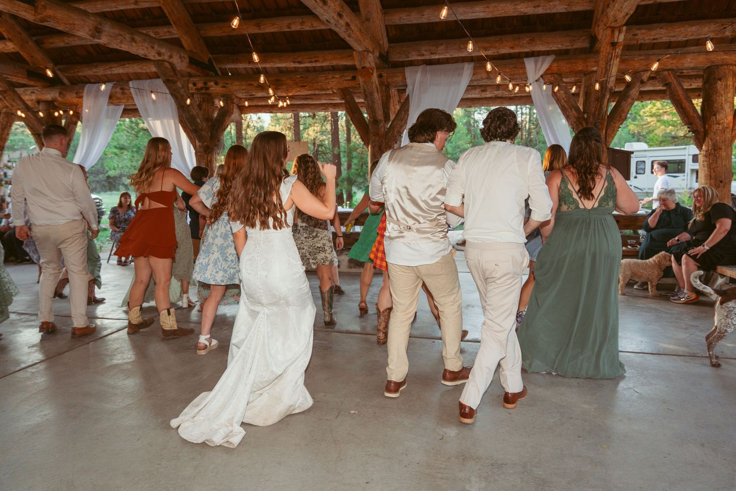 Wedding guests dancing together at a rustic outdoor venue with string lights overhead.