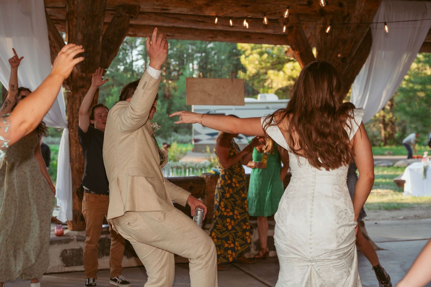 Wedding reception dance floor filled with guests celebrating under wooden beams and string lights.