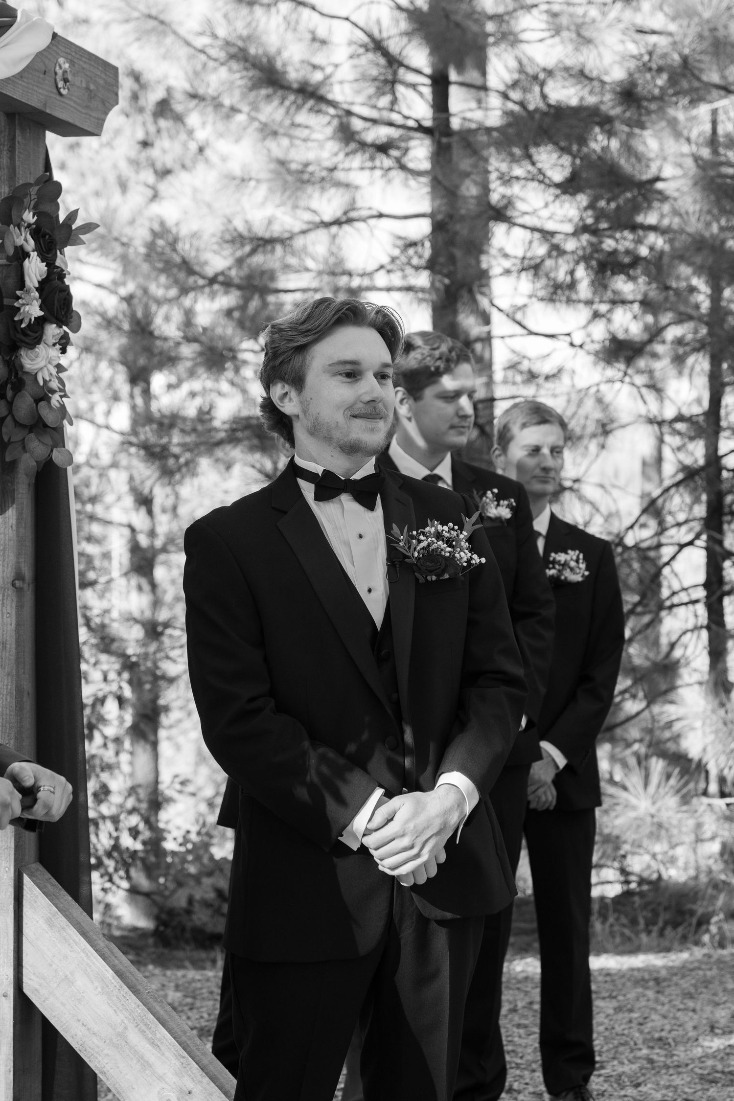Groomsmen in tuxedos stand at attention during forest wedding ceremony.